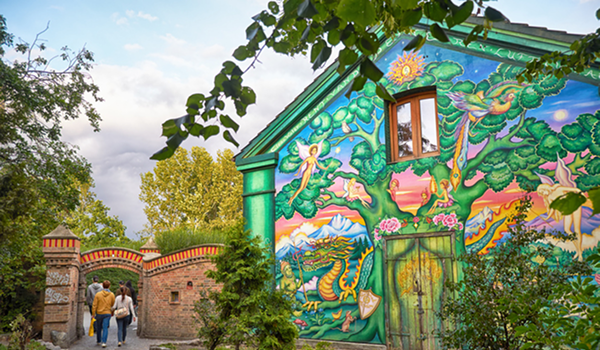 Vchod do Christianie v Kodani s výrazným, farebným, rozprávkovým muralom na budove, obklopeným zeleňou.