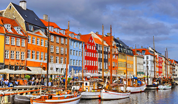 Ikonický prístav Nyhavn v Kodani s historickými lodičkami a dlhým radom farebných meštianskych domov pod zamračenou oblohou.