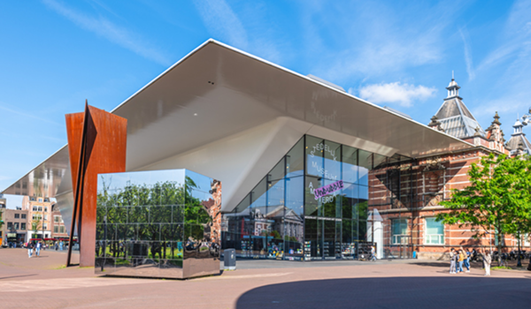 Moderná architektúra: Vonkajší pohľad na Stedelijk Museum v Amsterdame s futuristickou bielou strechou a lesklým zrkadlovým kubusom pred vchodom.