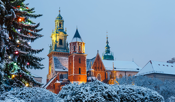 Zimný advent v Krakove ukazuje zasnežený hrad Wawel s veľkým osvetleným vianočným stromčekom v popredí.