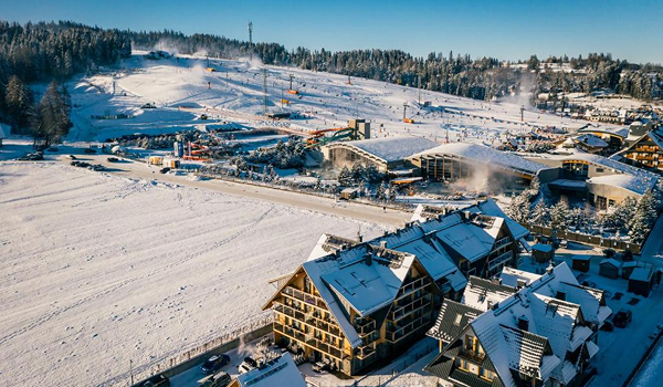 Letecký záber na zimné stredisko Białka Tatrzańska, zachytávajúci termálne kúpalisko Terma Bania s vonkajšími bazénmi v tesnej blízkosti lyžiarskych svahov a hotelov.