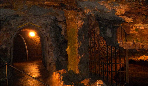 Tajomný interiér travertínovej jaskyne pod Bojnickým zámkom s kamennými stenami a osvetleným podzemným priechodom.