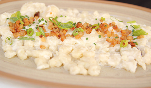 Detail tradičného slovenského jedla Bryndzové halušky s bryndzou, posypané opečenou slaninou a čerstvou pažítkou na tanieri.