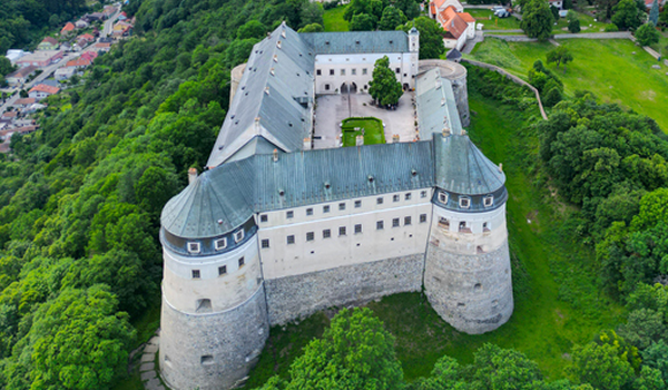 Pohľad z vtáčej perspektívy na majestátny Hrad Červený Kameň s mohutnými hradbami, vežami a vnútorným nádvorím, obklopený lesmi.