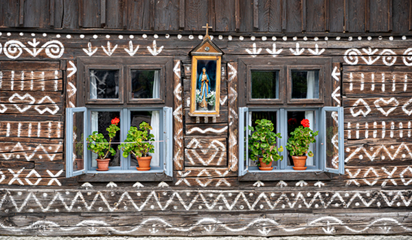 Detail tradičnej drevenice z Čičmian s charakteristickou bielou geometrickou ornamentálnou maľbou okolo okien a mariánskym výklenkom.