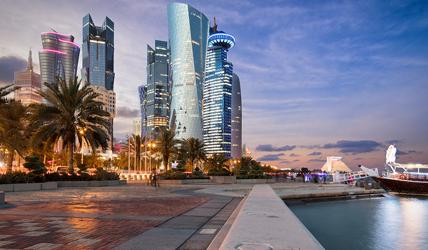 Moderná panoráma mrakodrapov v časti West Bay v Dauhe pri súmraku, s výhľadom z promenády a loďkou v popredí.