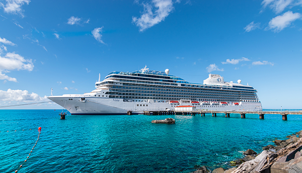 Luxusná výletná loď kotviaca v prístave pri drevenom móle s tyrkysovou vodou a modrou oblohou v exotickej destinácii.