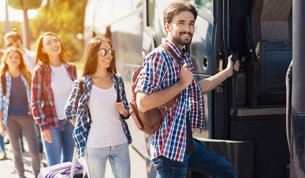 Skupina usmievavých mladých ľudí s kuframi a batohmi radostne nastupuje do moderného zájazdového autobusu.
