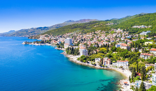 Panoramatický záber na prímorské mesto Opatija s hotelmi na zelených svahoch lemujúcich tyrkysové more.