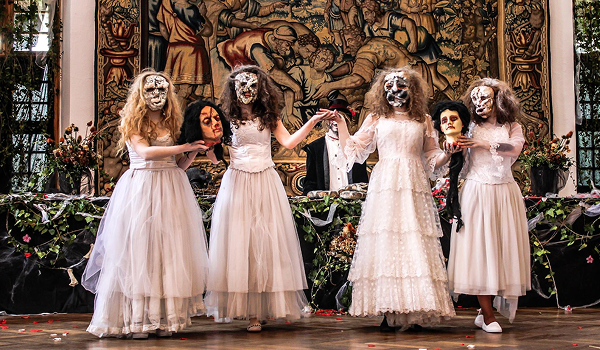 Herci v bielych kostýmoch a strašidelných maskách pózujúci s rekvizitami počas Medzinárodného festivalu duchov a strašidiel na Bojnickom zámku.