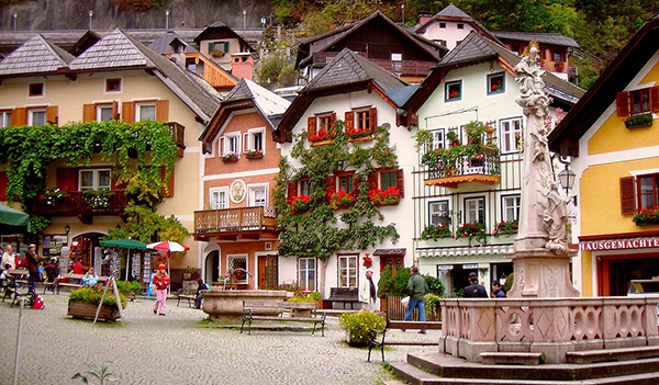 Historické námestie v Hallstatte s farebnými domami, kvetinovou výzdobou a centrálnou kamennou fontánou.