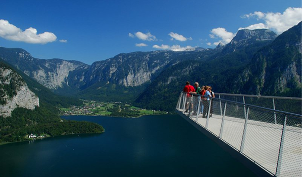 Turisti na visutej vyhliadkovej plošine Skywalk s dychberúcim výhľadom na Halštatské jazero a okolité alpské vrcholy.