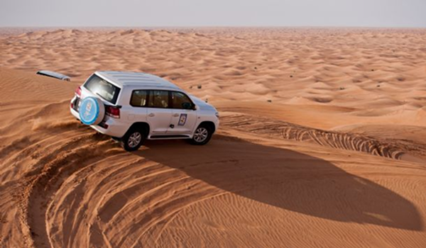 Biele terénne auto pri adrenalínovej jazde po piesočných dunách v púšti v blízkosti Dauhy v Katare.