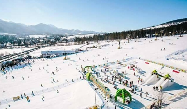 Slnečný pohľad na širokú, miernu zjazdovku pre začiatočníkov s vyhradenou detskou zónou a hernými prvkami v lyžiarskom stredisku.