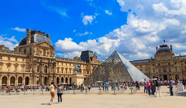 Sklenená pyramída a historické budovy múzea Louvre v Paríži plné turistov počas poznávacieho zájazdu.