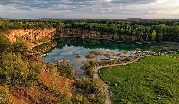 Panoráma zatopeného lomu so zelenými lesmi a skalnatými útesmi ukazuje obľúbenú turistickú atrakciu Park Gródek v Poľsku.