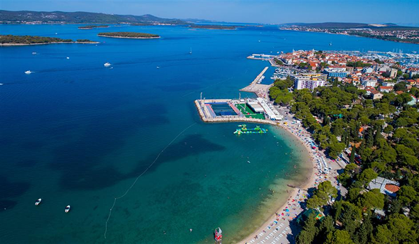 Plaža Dražica v Biograde na Moru, Chorvátsko, kombinuje prírodný tieň borovíc, upravené pobrežie a blízkosť mesta.