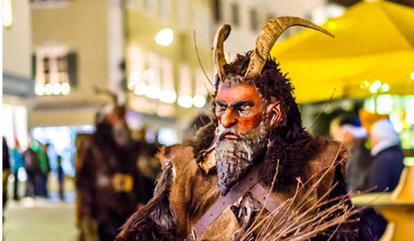 Tradičný Krampus z Mariazellu s tmavou bradou a rohom, odetého v kožuchu, s typickým zväzkom prútov.