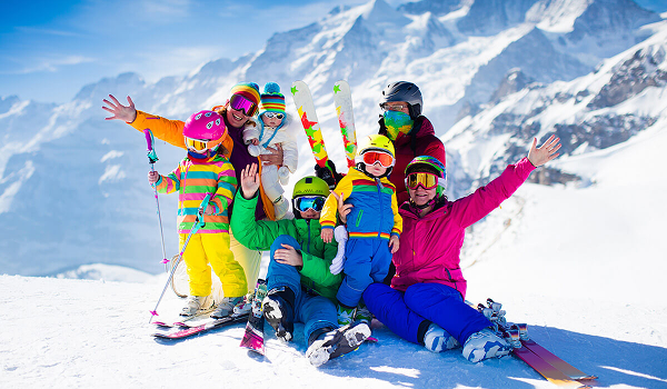 Šťastná rodina s deťmi v farebných lyžiarskych kombinézach pózuje na zasneženom svahu.