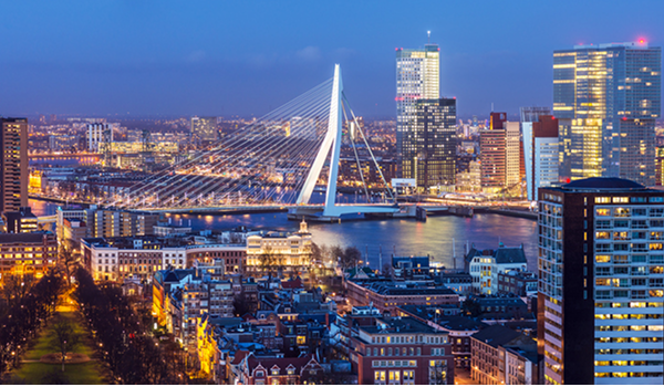Nočná panoráma moderného Rotterdamu s osvetlenými mrakodrapmi a výrazným bielym mostom Erasmusbrug nad riekou Maas.