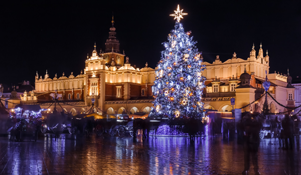 eľký osvetlený vianočný stromček s hviezdou dominuje nočnému námestiu s historickou budovou Sukiennice v Krakove.