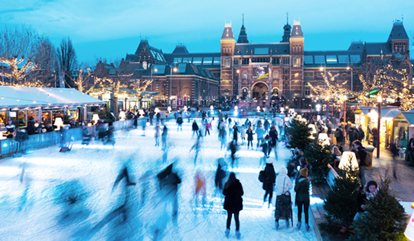 Zimná scéna z Amsterdamu: Ľudia korčuľujú na ľadovej ploche na Museumplein s historickou budovou Rijksmuseum v pozadí počas vianočných trhov.
