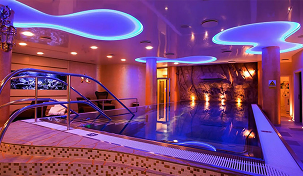 Exkluzívny vnútorný wellness bazén s modrým podsvietením a kamennou stenou určený na relaxačný pobyt.
