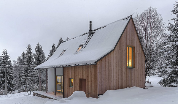 moderná drevená chata so snehom na streche, ideálna pre zimnú dovolenku.